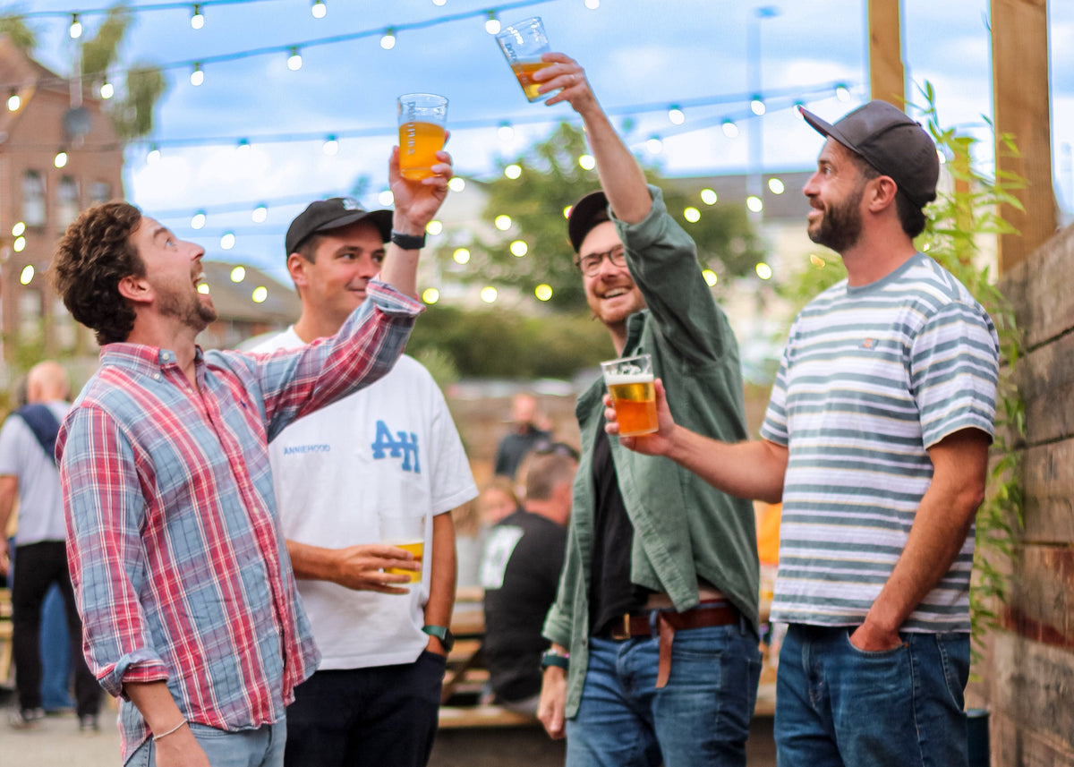 Four friends raising pints in a sunny pub garden