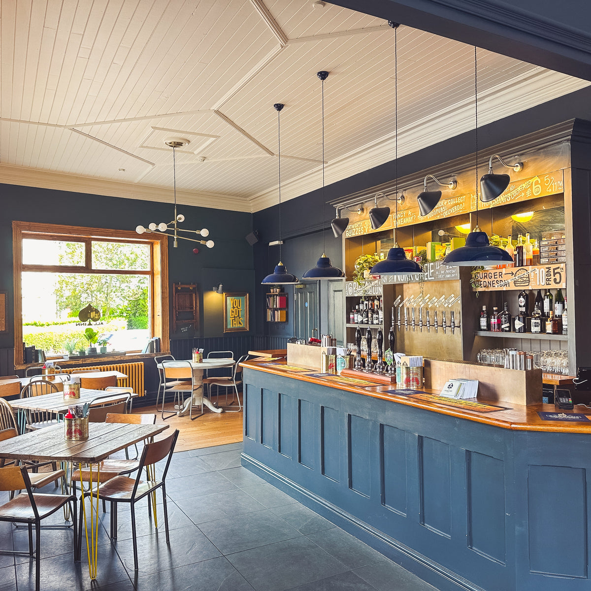 Blue-panelled pub bar with wooden tables and pendant lights
