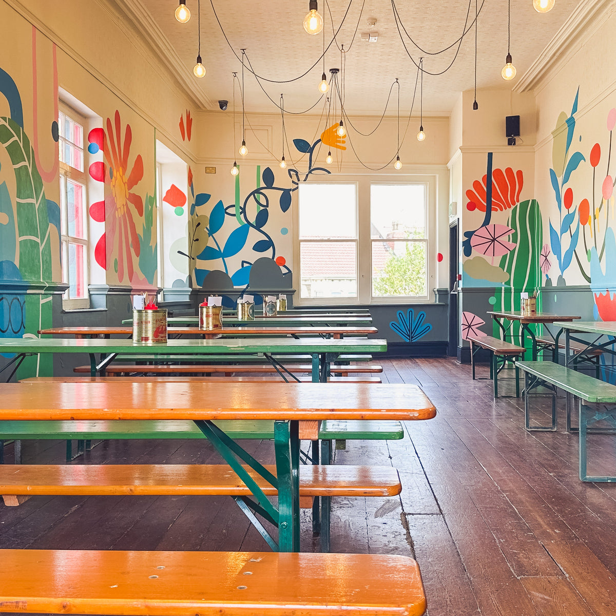 Bright dining room with long wooden benches and colourful painted floral murals