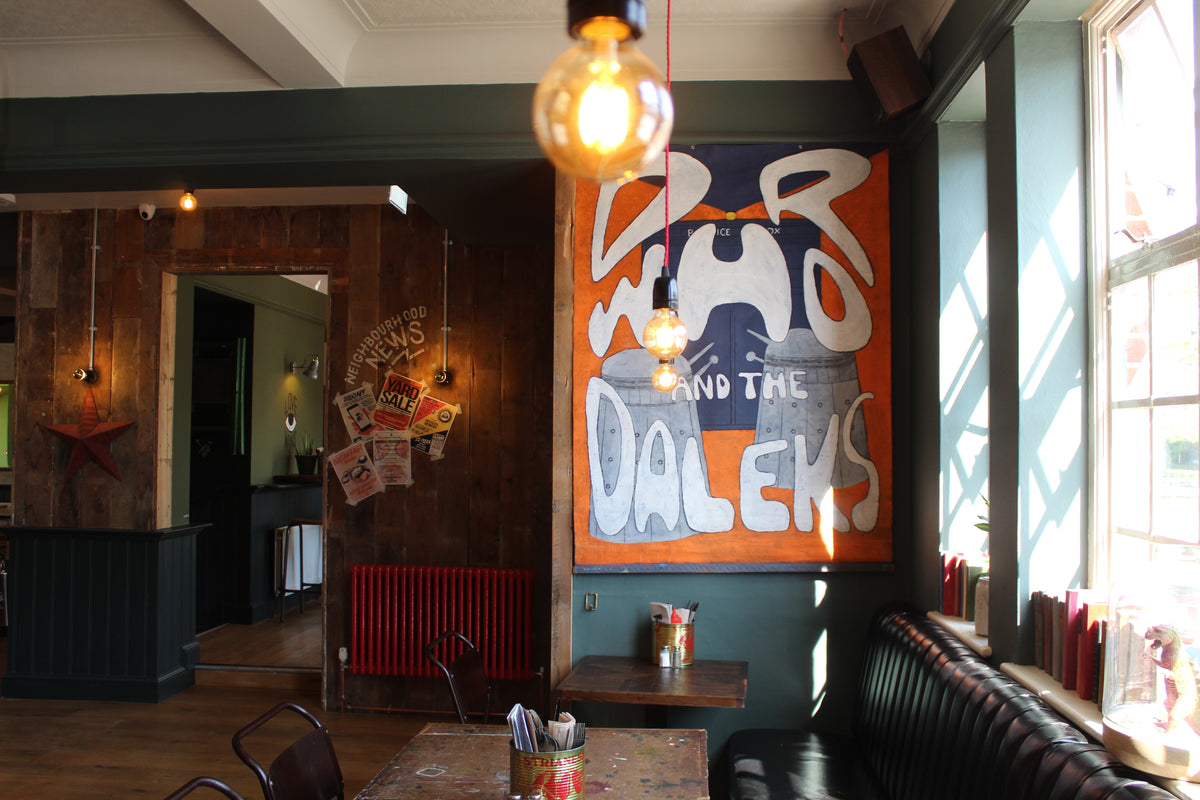 Interior of The Up In Arms with window seating and a large vintage Doctor Who and the Daleks poster
