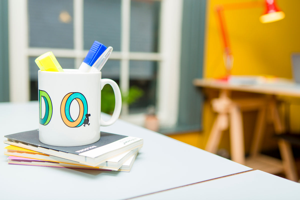 Dodo mug holding pens on a stack of notebooks on a desk
