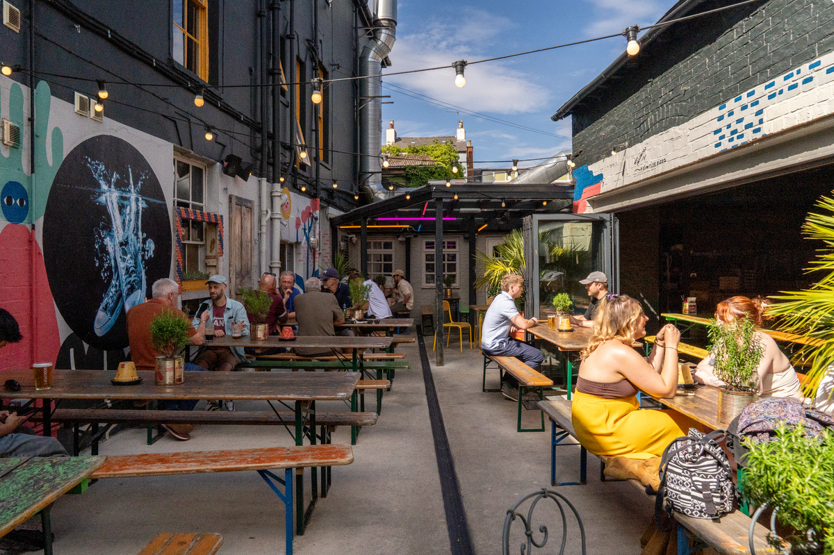 Sunny pub courtyard with festoon lights, wooden benches and a large painted mural