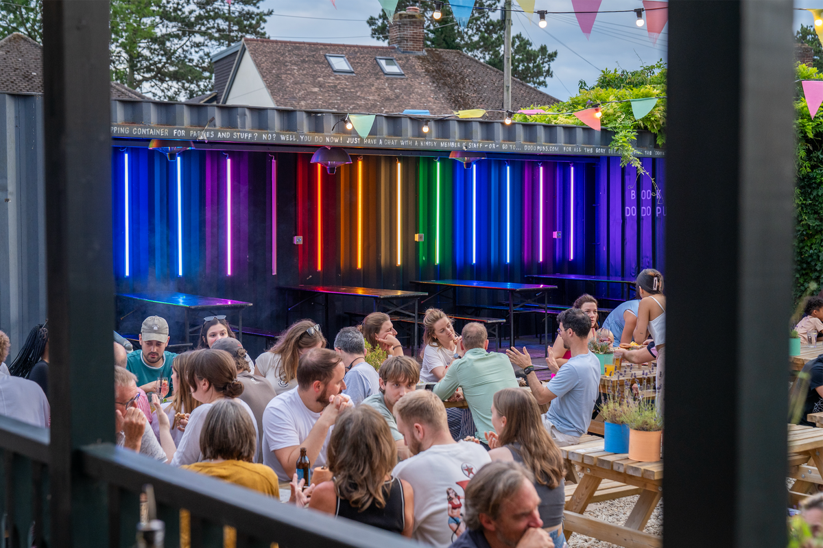 Busy beer garden at The Up In Arms in front of rainbow-lit booths
