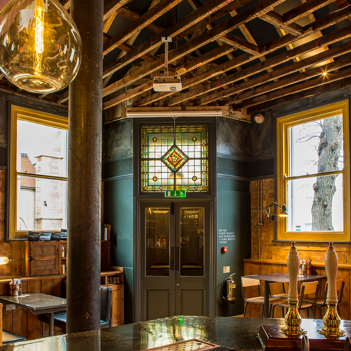 Interior of a rustic pub with wooden beams, stained glass door, and vintage decor.