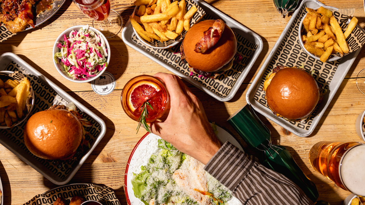 Overhead view of burgers, fries, salads and drinks shared on a wooden table