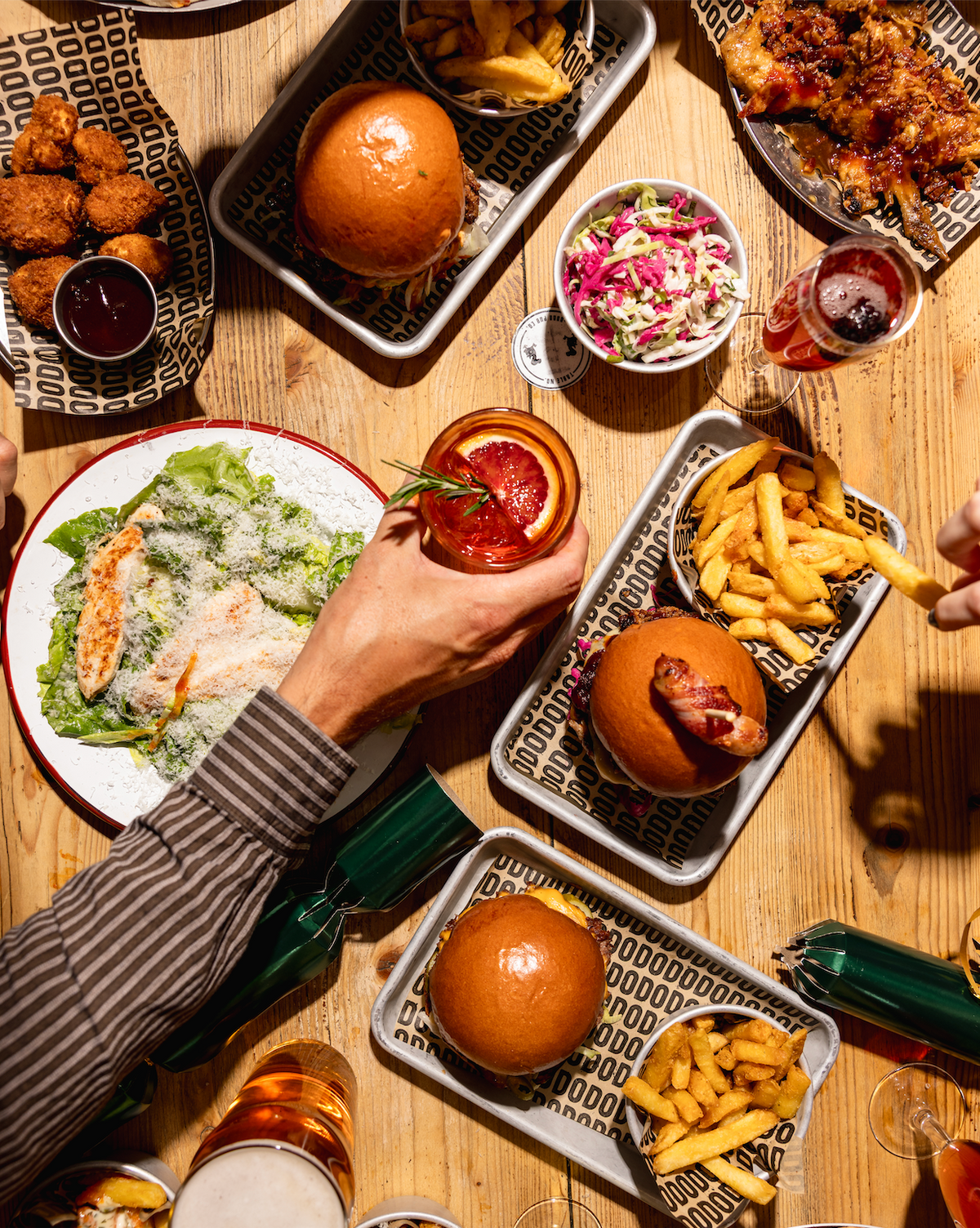 Overhead view of burgers, fries, salads and drinks shared on a wooden table