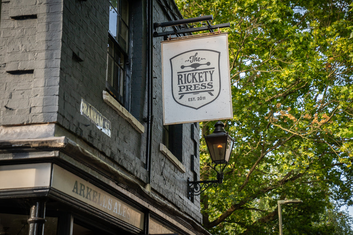 Hanging sign for The Rickety Press on the corner of a brick building