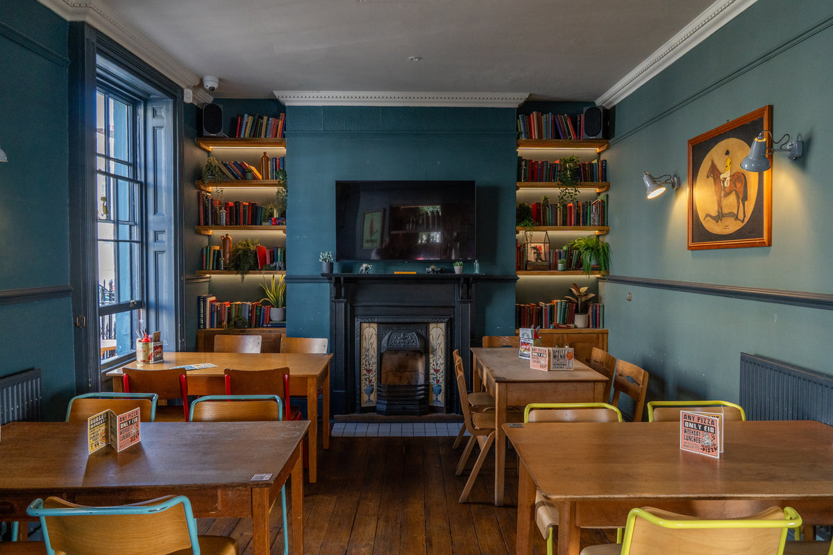 Pub dining room with wooden tables, a fireplace and bookshelves