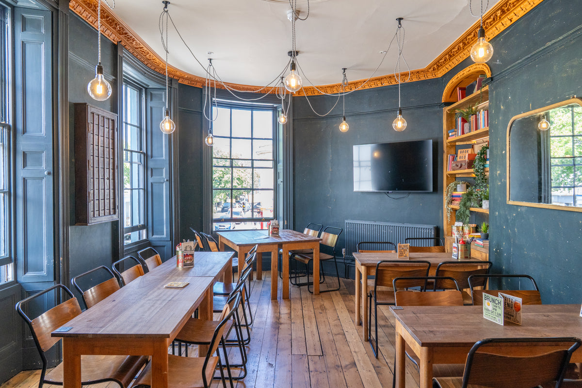 Blue-walled dining room with long wooden tables and festoon lights