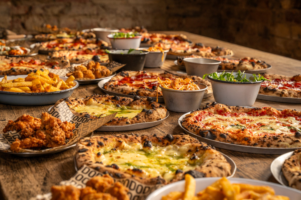 Wood-fired pizzas, fries and wings laid out across a long wooden table