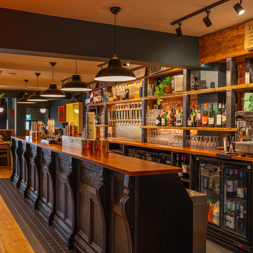 Long carved wooden bar with beer taps and shelves of spirits at The High Horse