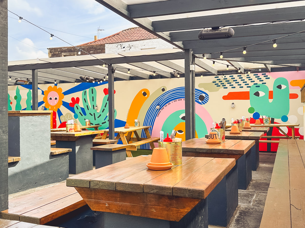 Covered roof terrace with wooden tables and a colourful painted mural