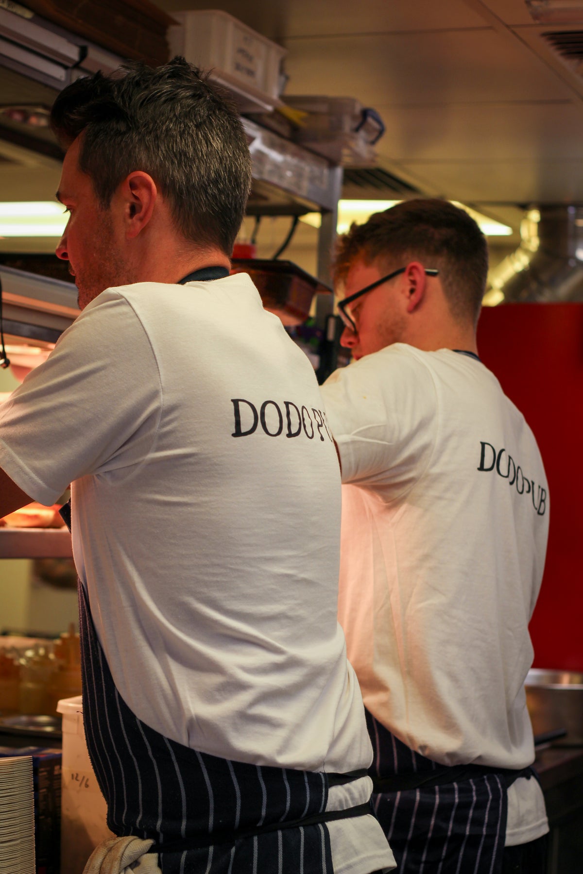Two Dodo chefs in branded T-shirts and aprons working in the kitchen