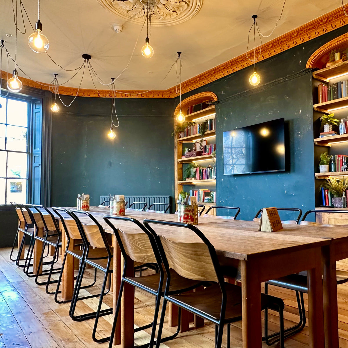 Long table and bookshelves in a blue-walled dining room at The Airs & Graces
