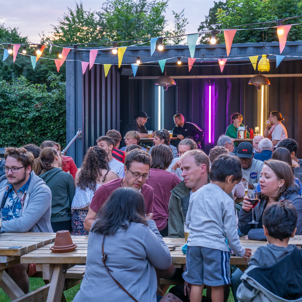 Families and friends at picnic tables in the beer garden at The Last Crumb, decorated with bunting