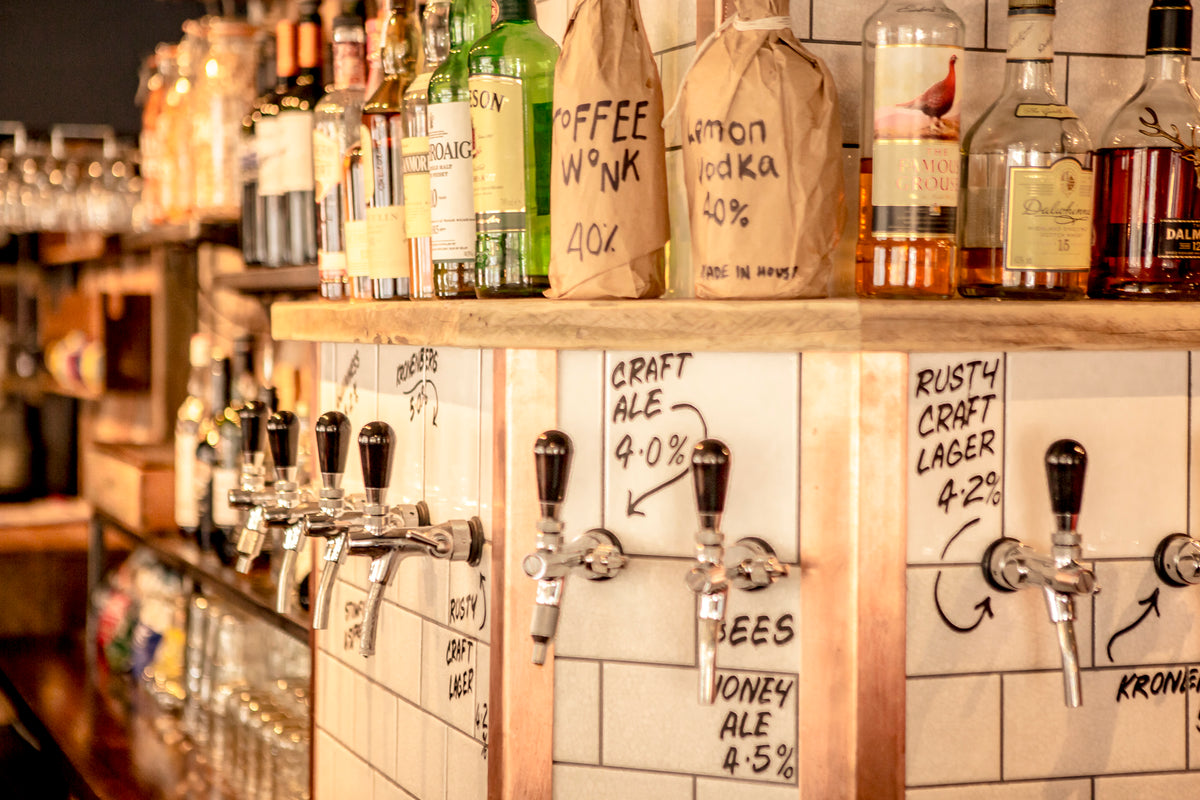 Row of beer taps and hand-labelled spirits behind a tiled bar