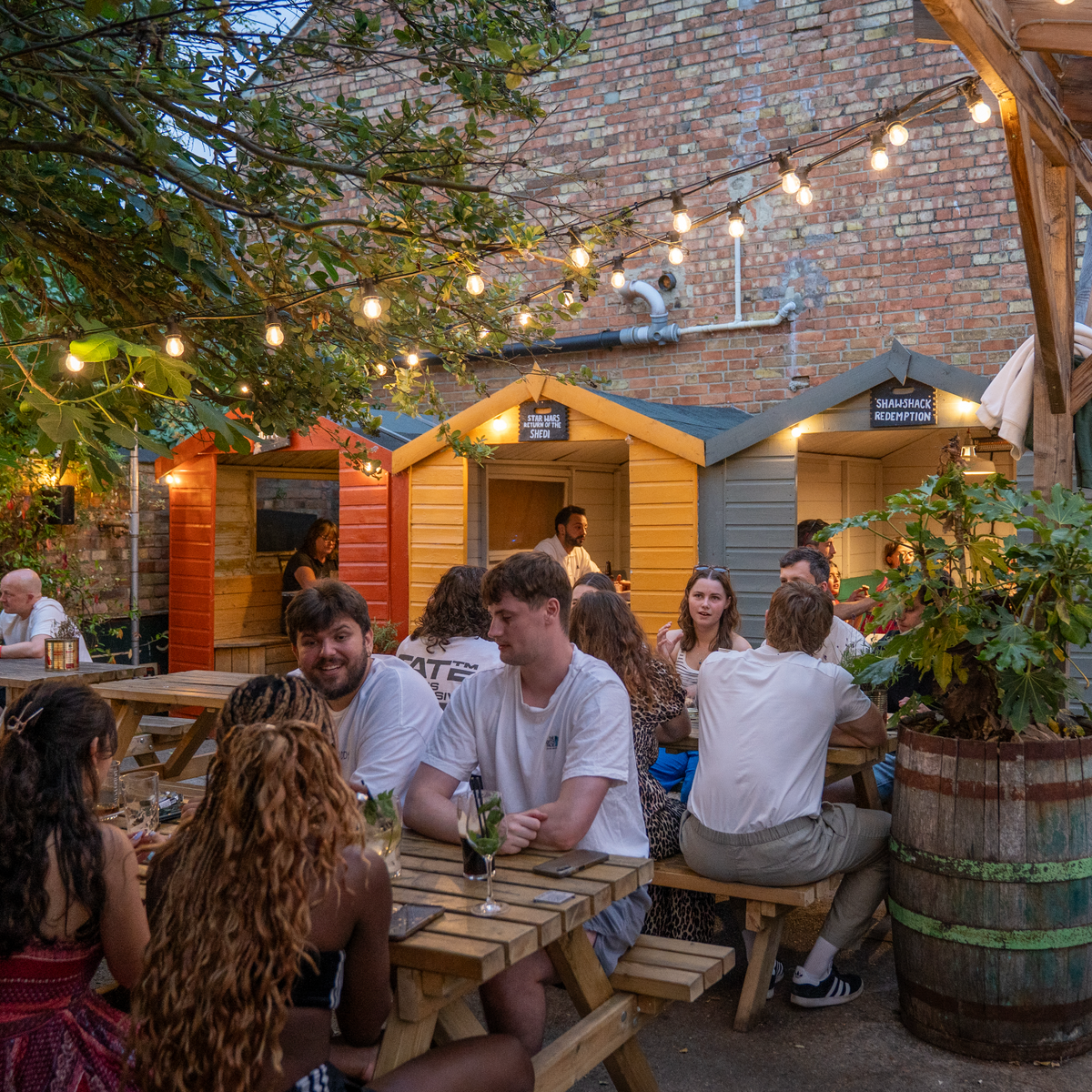 Busy beer garden at The Rusty Bicycle with festoon lights and colourful beach-hut booths