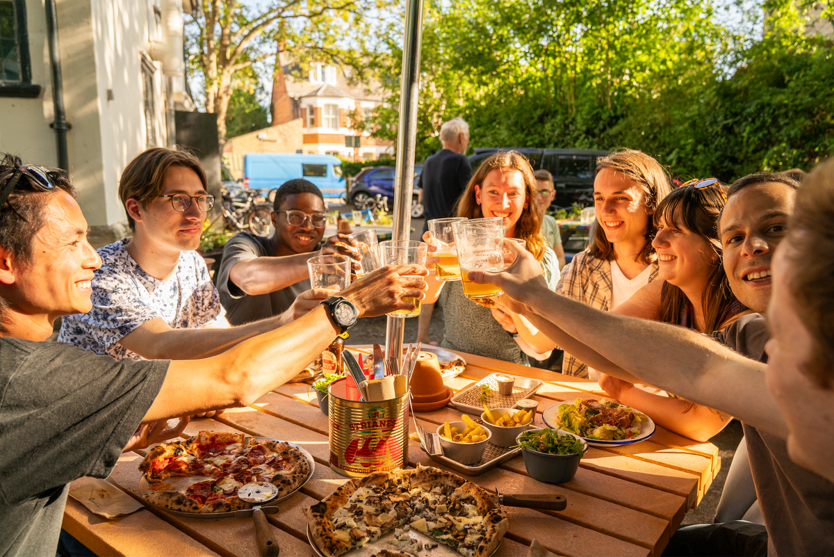 Friends toasting with drinks over pizzas at an outdoor table