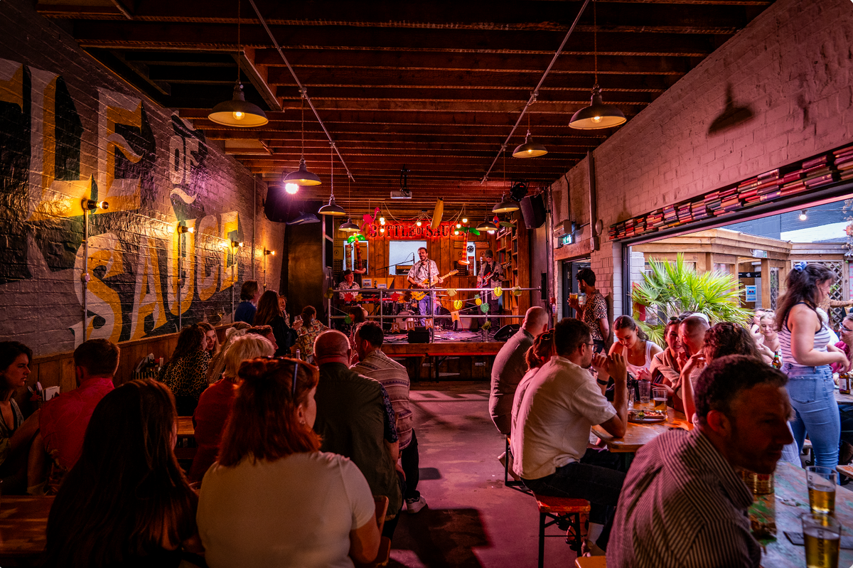 Busy evening crowd inside The Bottle of Sauce with live music at the back