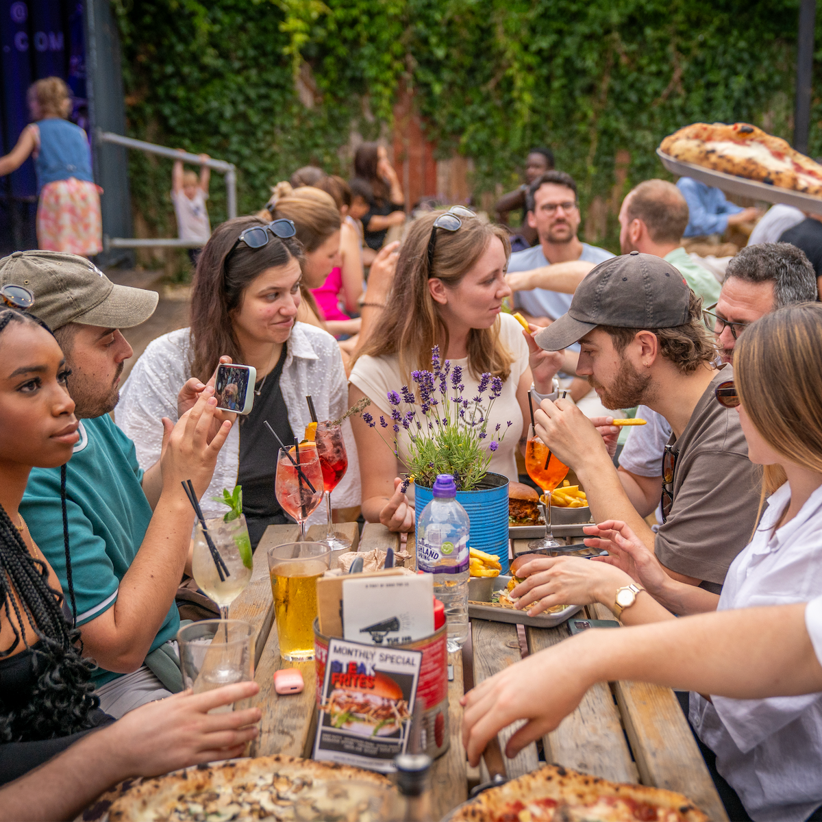 Friends sharing pizzas and drinks around a table at The Up In Arms